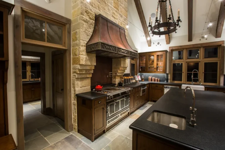 Темная деревянная кухня в кантри стиле, встроенная в стену с порталом каминного типа из крупного камня