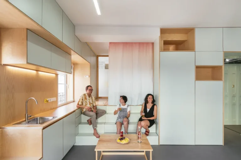 Мужчина и 2 женщины сидят на ступеньках, ведущих из кухонной зоны в спальную зону студии