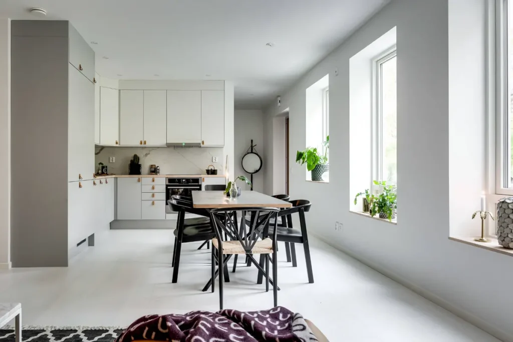 Угловая кухня-гостиная под потолок с бело-серыми фасадами и кожаными ручками