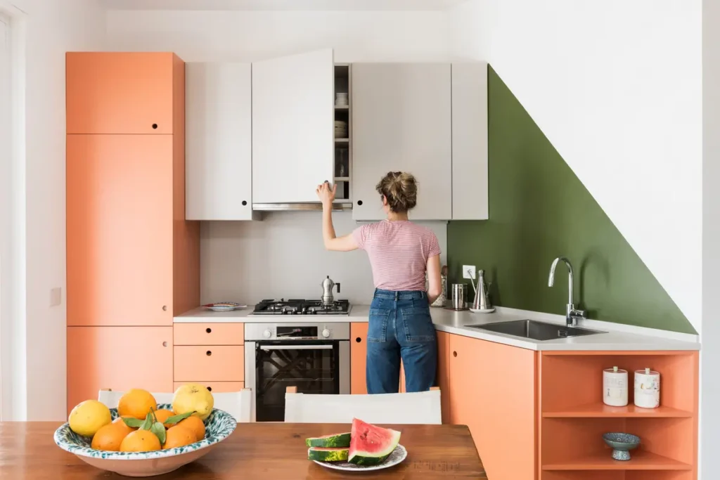 Женщина открывает дверку навесного шкафа кухонного гарнитура с серыми и оранжевыми фасадами