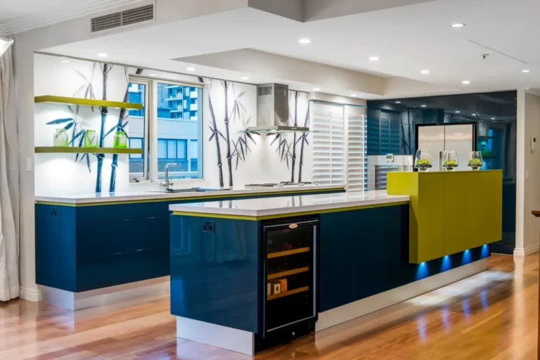 Блестящий интерьер кухни с гарнитуром и островом в синих и зеленых оттенках, стеклянной стеновой панелью